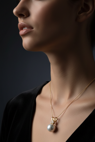 Close-up of a woman wearing a gold necklace with a pearl pendant against a dark background