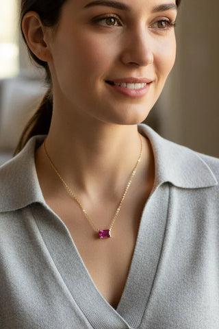 Woman wearing a gold necklace with a red gemstone in a neutral setting