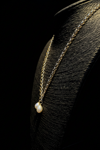 Gold necklace with a pearl pendant on a black background