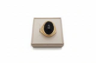 Gold ring with a black stone on a white box against a gold background