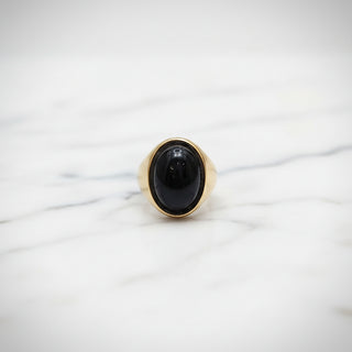 Gold ring with a black gemstone on a reflective gold surface
