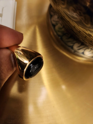 Gold ring with a black stone held by a hand on a reflective surface