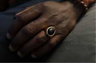 Hand wearing a ring with a black gemstone on a gray surface