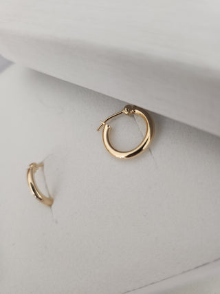 A pair of polished gold huggie hoop earrings displayed on a white textured jewelry box.