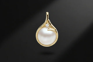 Gold pendant with a white pearl and small diamond accent on a black background