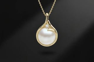Gold necklace with round pearl pendant and small diamond accent on black background