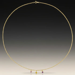 Gold necklace with small colored charms on a gradient background