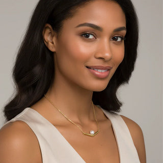 Woman wearing a gold necklace with a pearl pendant against a neutral background