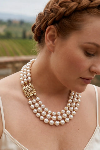 Close-up of a woman wearing a multi-strand pearl necklace with a gold ornate clasp.