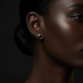 Close-up of a woman's ear wearing a gold earring against a dark background
