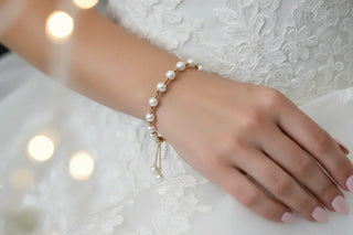 Bride wearing gold and pearl slider bracelet on lace wedding dress