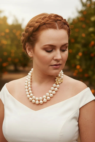 Woman with braided red hair wearing a double strand pearl necklace with a gold clasp.