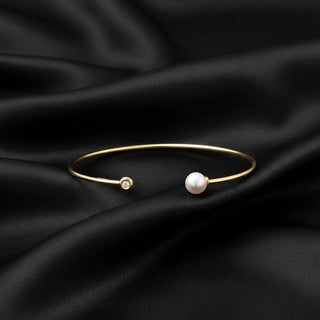 Gold cuff bracelet with pearl and diamond detail on black satin background