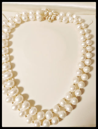 A double-strand pearl necklace with irregular white pearls and gold-toned spacers, displayed on a cream-colored surface.