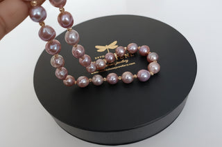Pink pearl necklace on a black jewelry box with a visible brand logo.