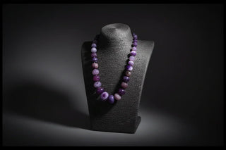 Necklace with purple beads on a dark stand against a black background