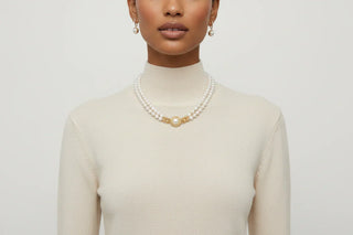 Person wearing a pearl necklace and earrings against a plain background
