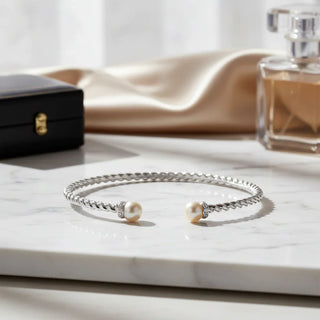 Elegant twisted silver bangle bracelet with pearl ends displayed on marble surface