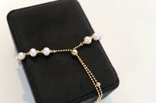 Gold chain pearl bracelet displayed on a black jewelry box, white background