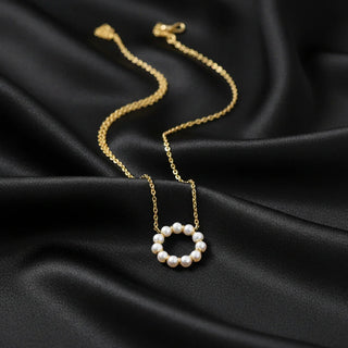 Gold necklace with a spring ring clasp and  circular pearl pendant on black fabric