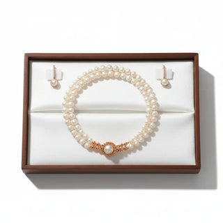 Double pearl necklace with gold clasp and matching earrings in a jewelry box on a white background
