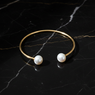 Gold bracelet with two pearls on a black marble surface