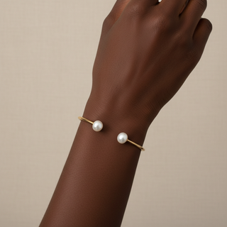 Gold bracelet with pearls on a wrist against a beige background
