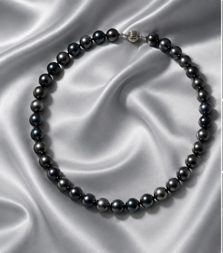A dark grey Tahitian pearl necklace on a white silk fabric 