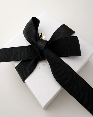 A white rectangular gift box tied with a wide black ribbon bow, photographed on a clean white background. 