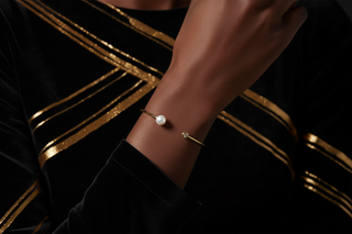 Gold bracelet with a pearl on a wrist against a dark background