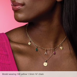 Woman wearing layered gold charm necklaces on a pink background