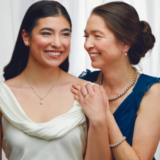 Two women standing close together, smiling and holding hands against a white background
