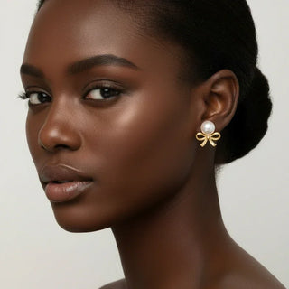 Woman wearing gold bow stud earrings with white pearls, elegant handcrafted jewelry