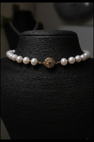 Elegant pearl necklace with gold filigree clasp, displayed on black mannequin for timeless luxury.