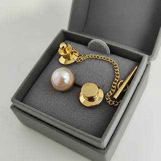 Gold cufflinks with a pearl and two gold buttons in a gray box on a light gray background