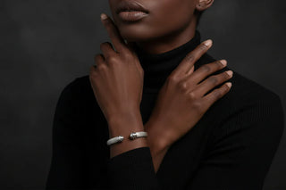 Person wearing a black turtleneck with a silver bracelet on a dark background