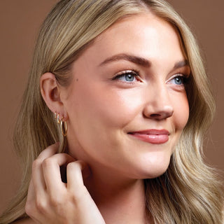 Woman wearing 14K yellow gold earrings with a brown background