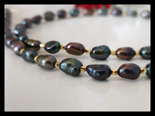 Handcrafted dark freshwater pearl necklace with gold spacer beads on a white surface.